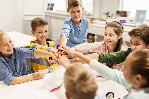 Children joining hands in a classroom, representing teamwork, unity, and shared values nurtured under the Parent-on-Campus model.